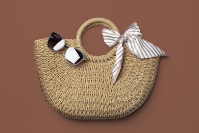 Image of Wicker bag and sunglasses on mocha mousse shade background, top view. Trendy color of 2025 year