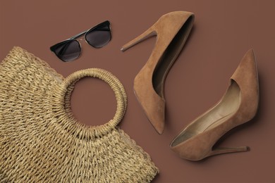 Image of Stylish shoes in mocha mousse shade, wicker bag and sunglasses on light brown background, flat lay. Trendy color of 2025 year