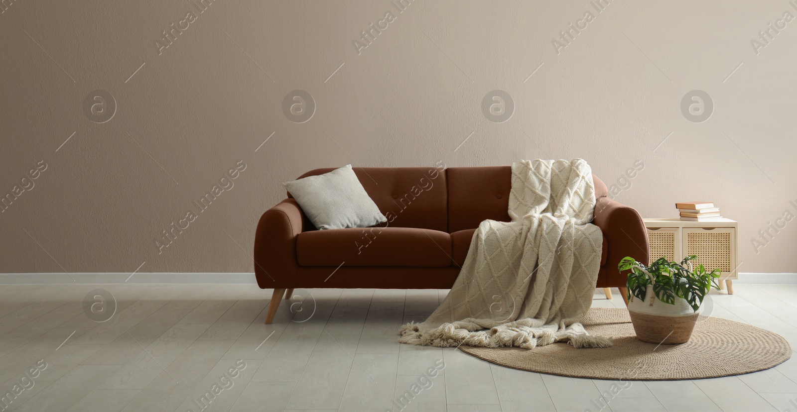 Image of Sofa in mocha mousse shade with blanket and pillow indoors. Stylish room interior with trendy color of 2025 year, banner design