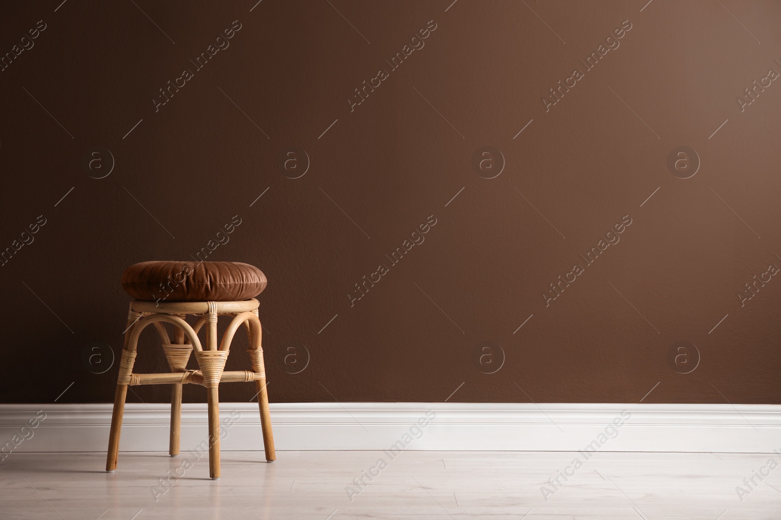 Image of Stylish rattan stool near wall in mocha mousse shade. Interior with trendy color of 2025 year