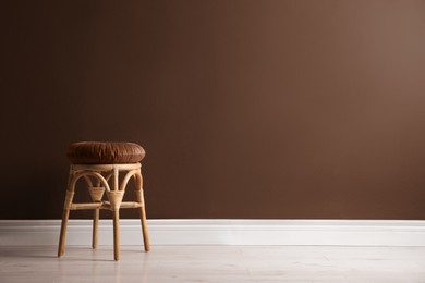 Image of Stylish rattan stool near wall in mocha mousse shade. Interior with trendy color of 2025 year