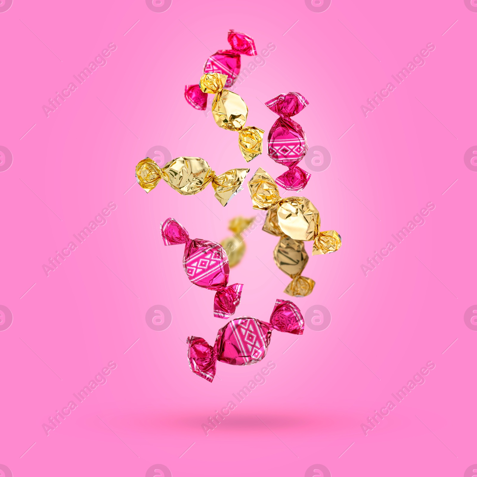 Image of Candies in bright wrappers falling on pink background