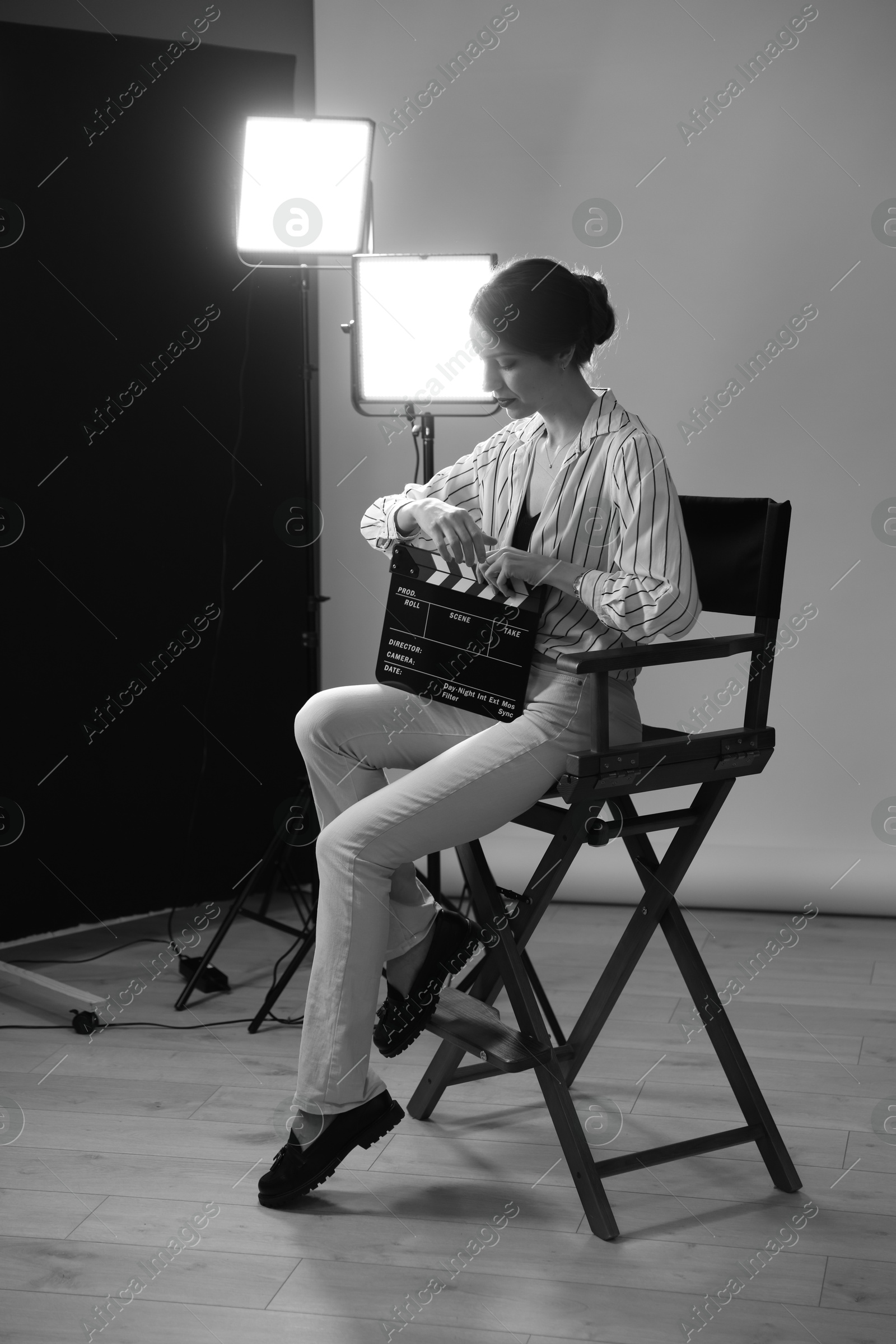 Photo of Beautiful woman with clapperboard sitting in director's chair in studio. Black and white effect