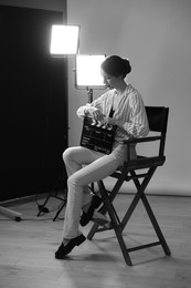 Photo of Beautiful woman with clapperboard sitting in director's chair in studio. Black and white effect