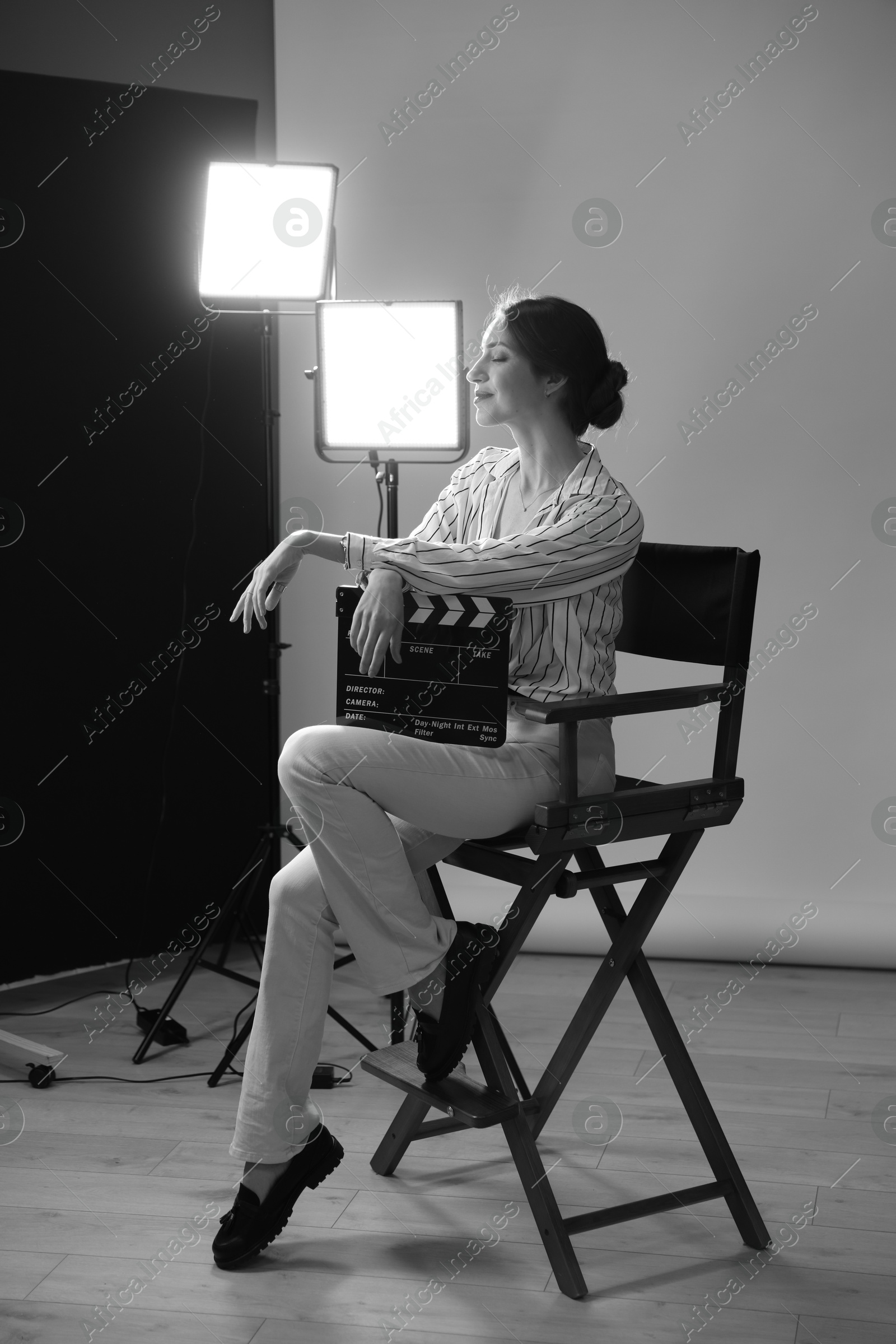 Photo of Beautiful woman with clapperboard sitting in director's chair in studio. Black and white effect