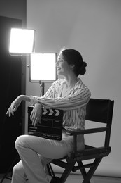 Photo of Beautiful woman with clapperboard sitting in director's chair in studio. Black and white effect