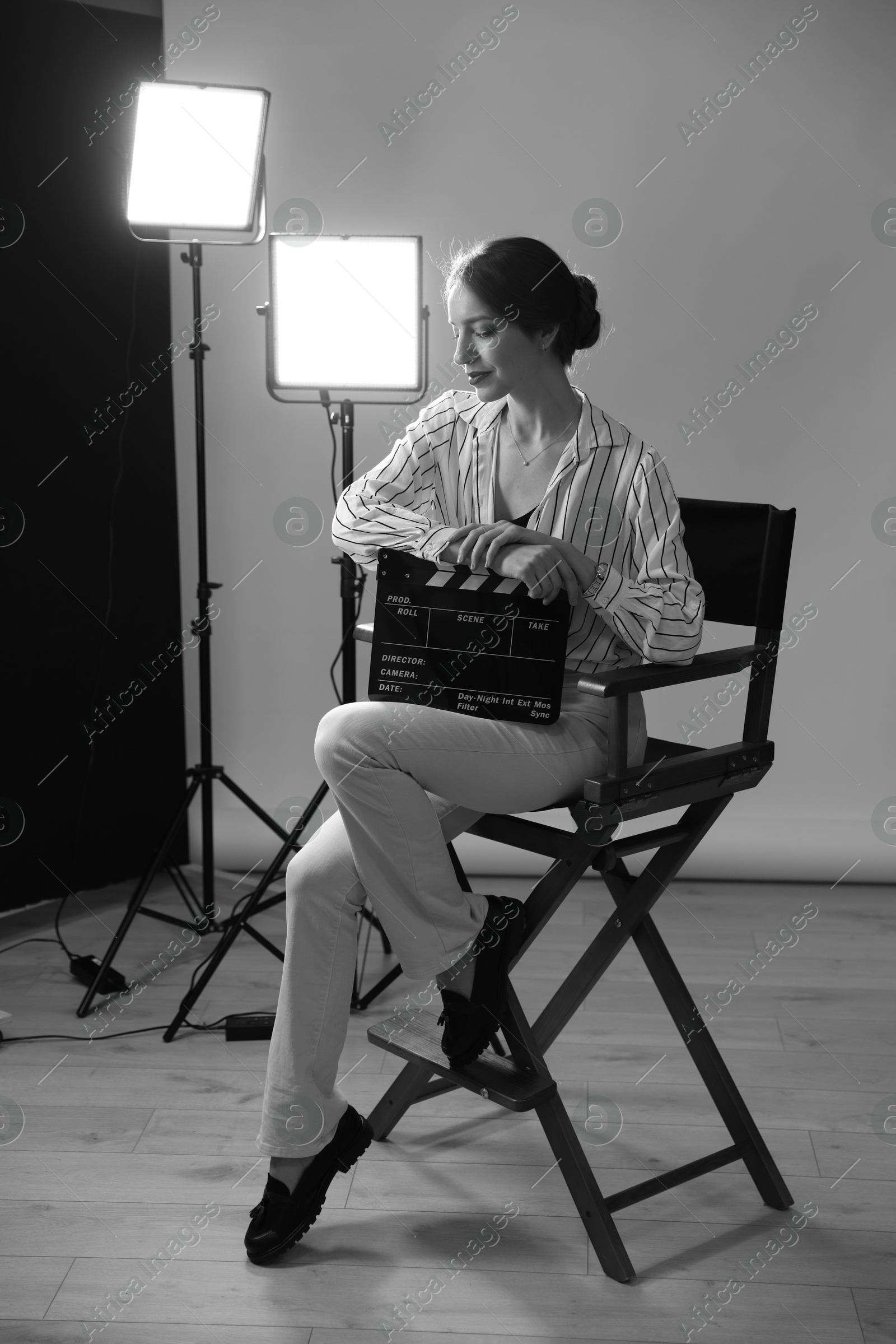 Photo of Beautiful woman with clapperboard sitting in director's chair in studio. Black and white effect