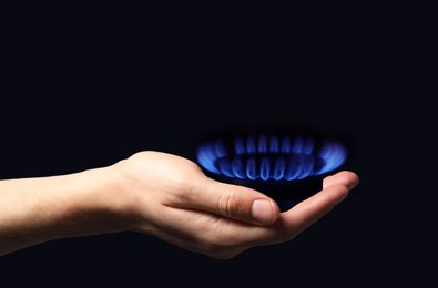 Image of Woman holding gas burner with blue flame on black background, closeup