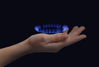 Woman holding gas burner with blue flame on black background, closeup