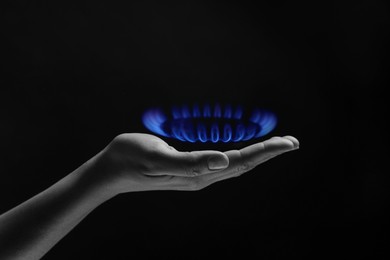 Woman holding gas burner with blue flame on black background, closeup. Black and white effect with color accent