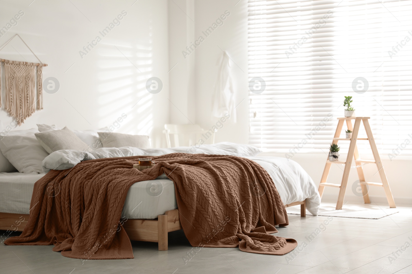 Image of Large bed with blanket in mocha mousse shade indoors. Stylish bedroom interior with trendy color of 2025 year