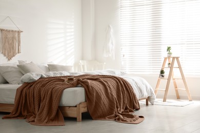 Image of Large bed with blanket in mocha mousse shade indoors. Stylish bedroom interior with trendy color of 2025 year