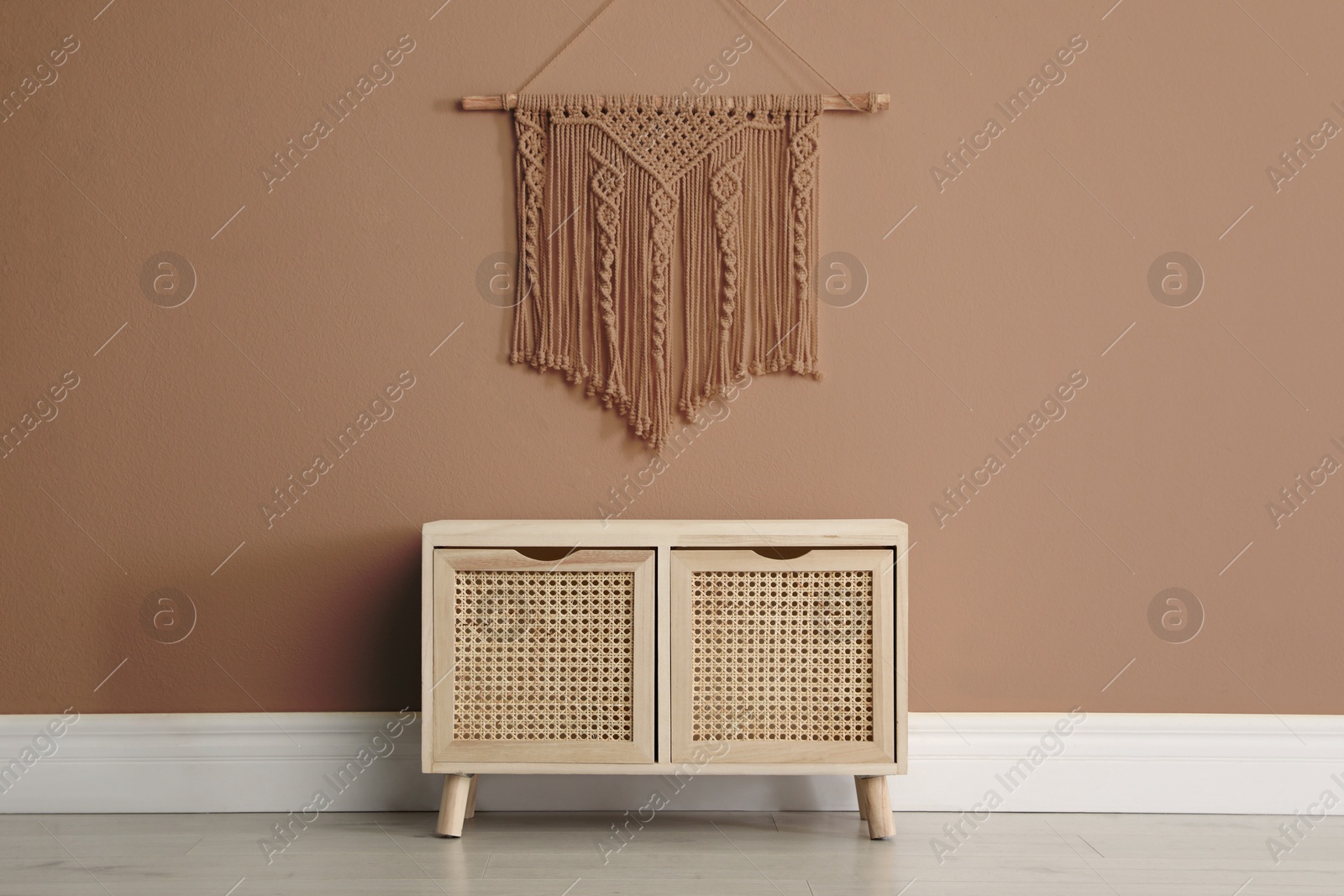 Image of Wooden commode and decor indoors. Wall in shade of mocha mousse. Stylish interior with trendy color of 2025 year