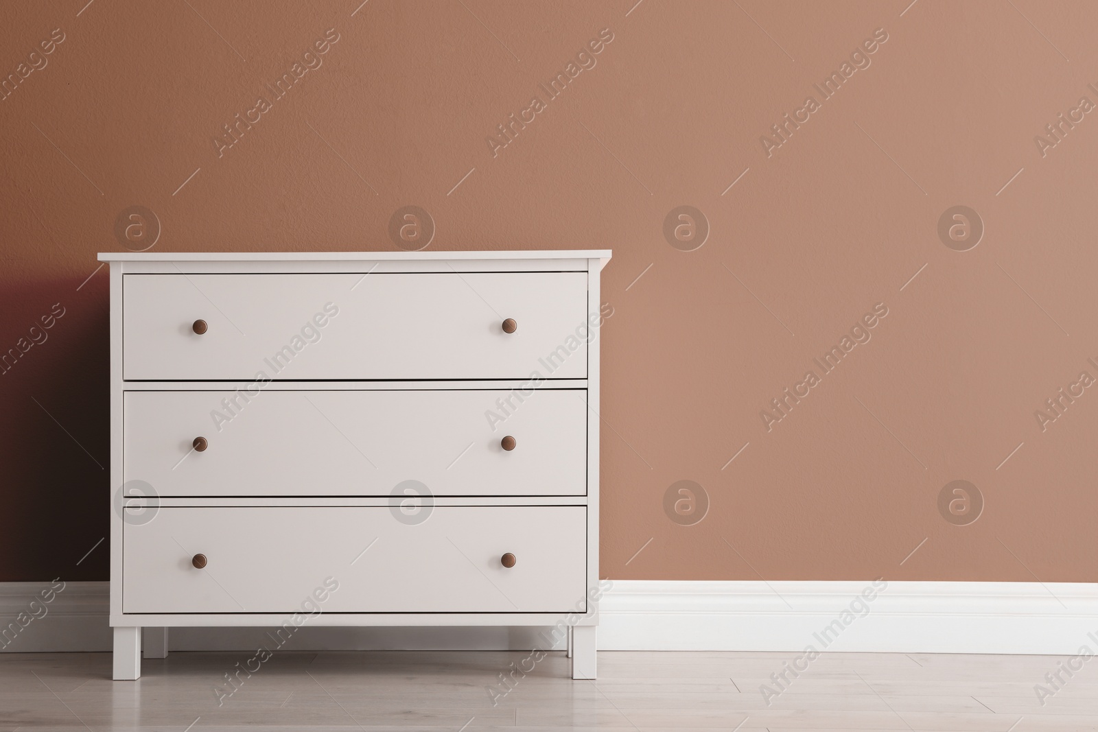 Image of Wooden chest of drawers near wall in shade of mocha mousse. Stylish interior with trendy color of 2025 year