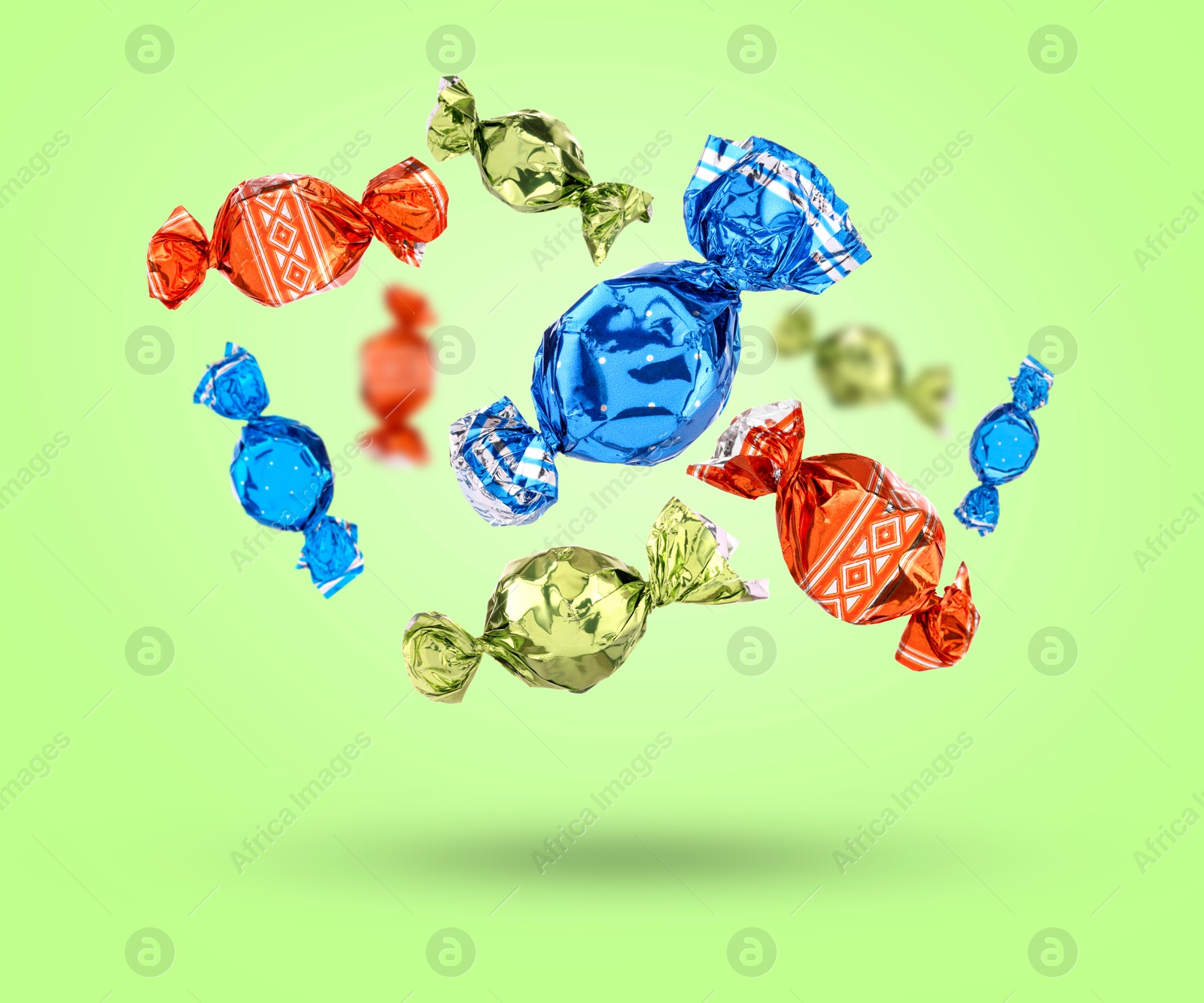 Image of Candies in bright wrappers falling on light green background