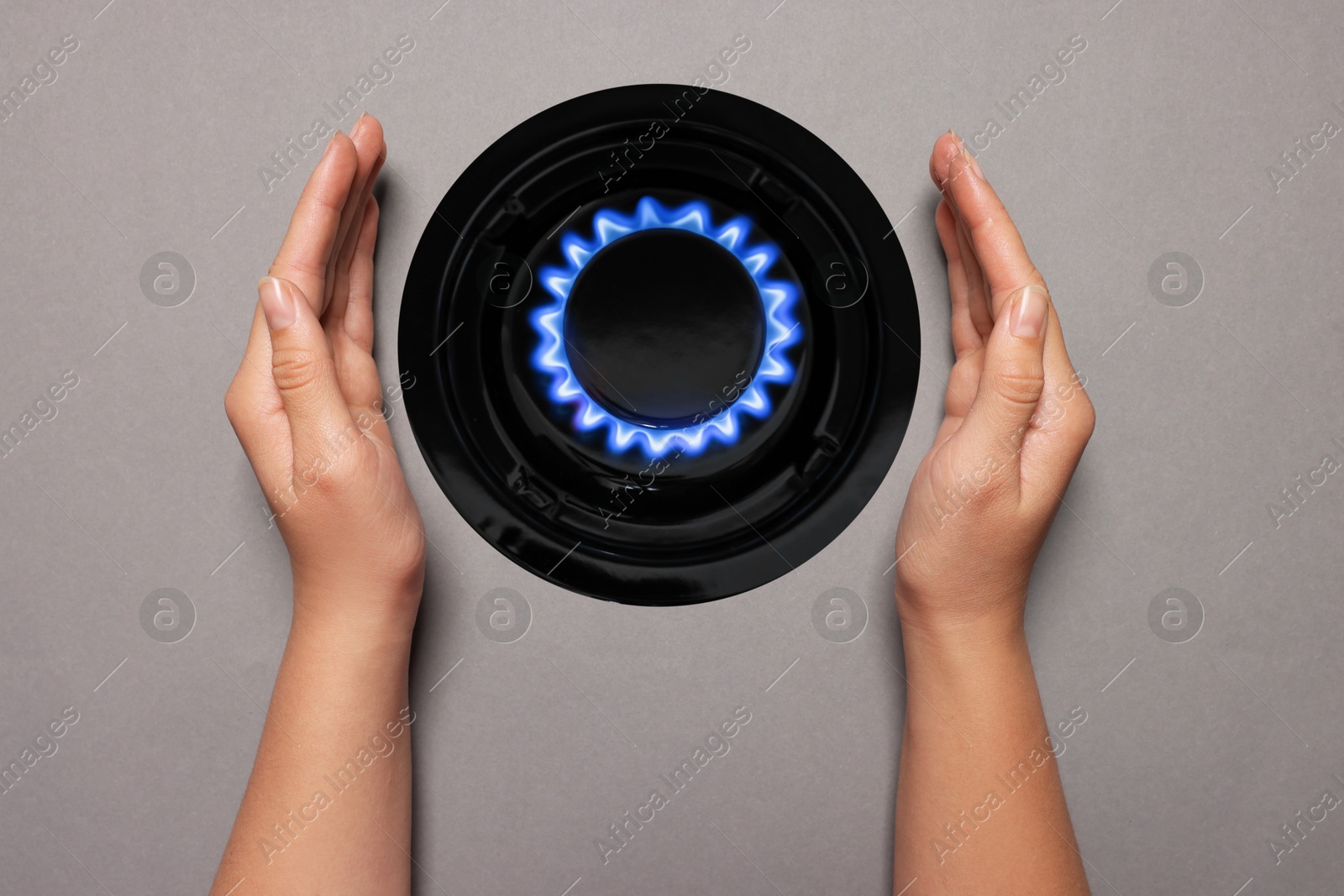 Image of Woman protecting gas burner with blue flame on grey background, top view