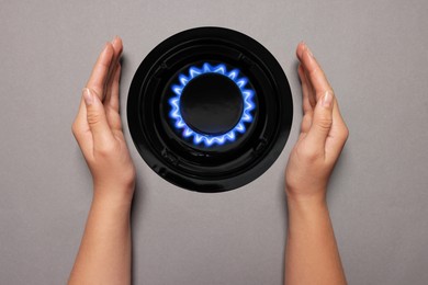 Image of Woman protecting gas burner with blue flame on grey background, top view