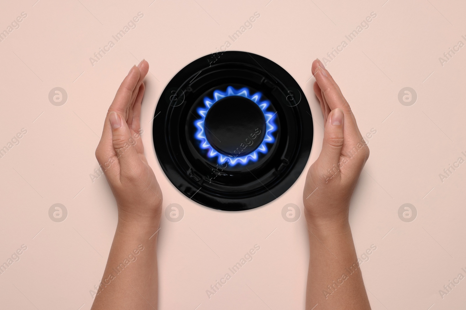 Image of Woman protecting gas burner with blue flame on pale pink background, top view