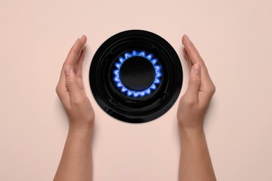 Image of Woman protecting gas burner with blue flame on pale pink background, top view