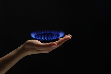 Image of Woman holding gas burner with blue flame on black background, closeup