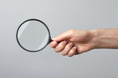 Photo of Woman holding magnifying glass on grey background, closeup. Find keywords concept