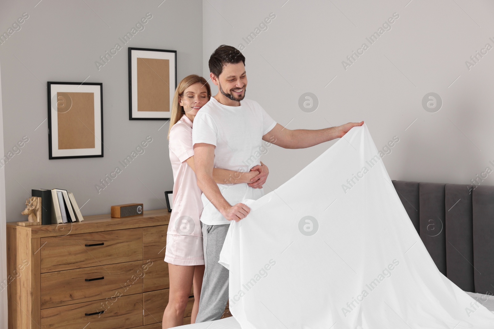 Photo of Couple changing bed linens in room. Domestic chores