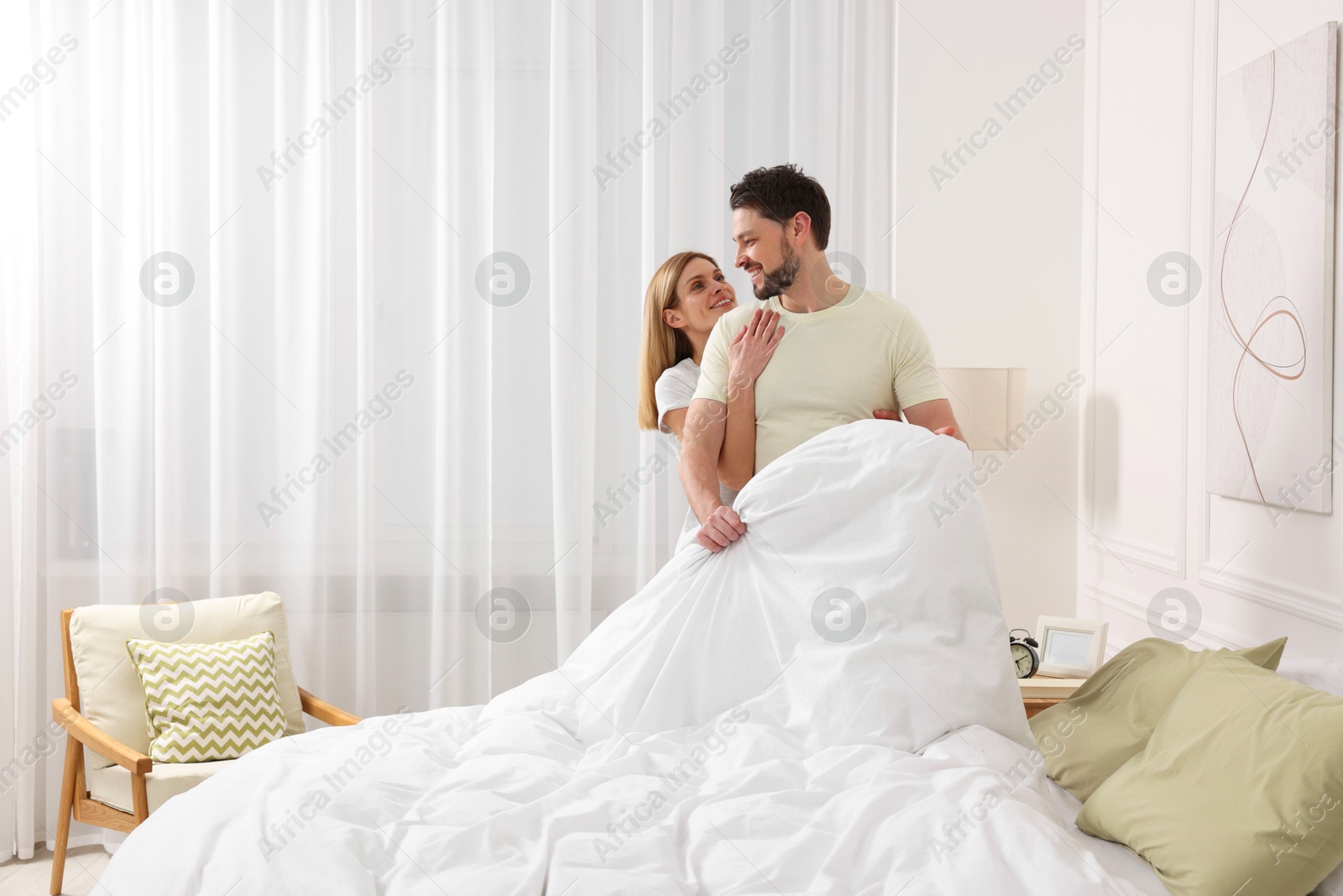 Photo of Couple changing bed linens in room. Space for text