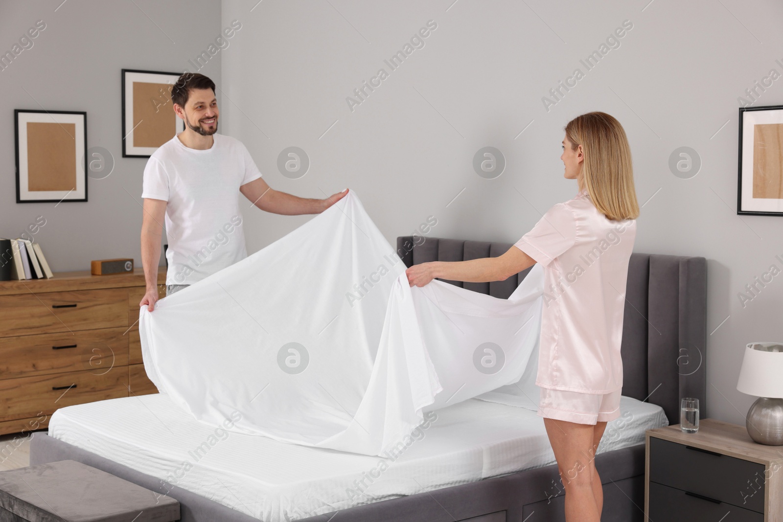 Photo of Couple changing bed linens in room. Domestic chores