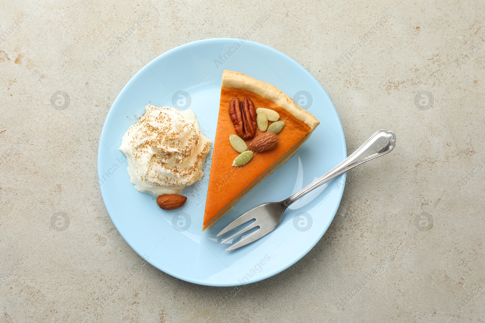 Photo of Piece of tasty homemade pumpkin pie with whipped cream, seeds and nuts on grey table, top view