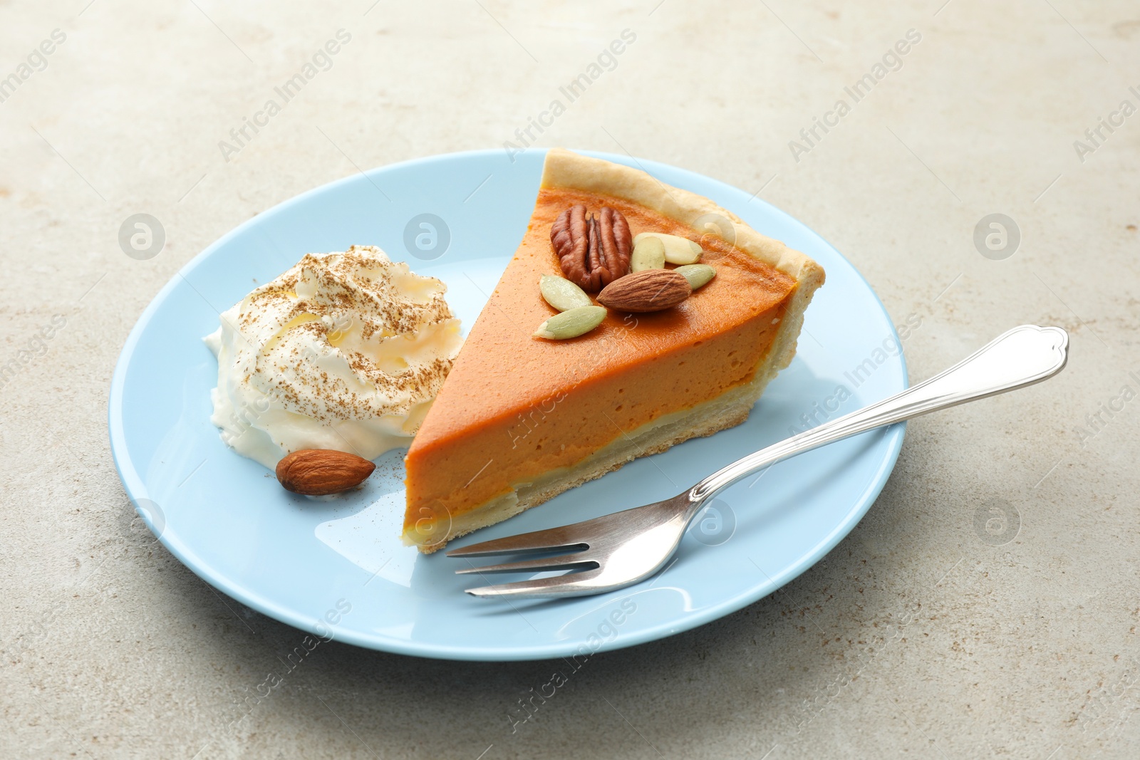 Photo of Piece of tasty homemade pumpkin pie with whipped cream, seeds and nuts on grey table, closeup