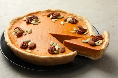 Photo of Tasty homemade pumpkin pie with seeds and nuts on grey table, closeup