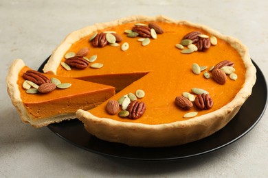 Photo of Tasty homemade pumpkin pie with seeds and nuts on grey table, closeup