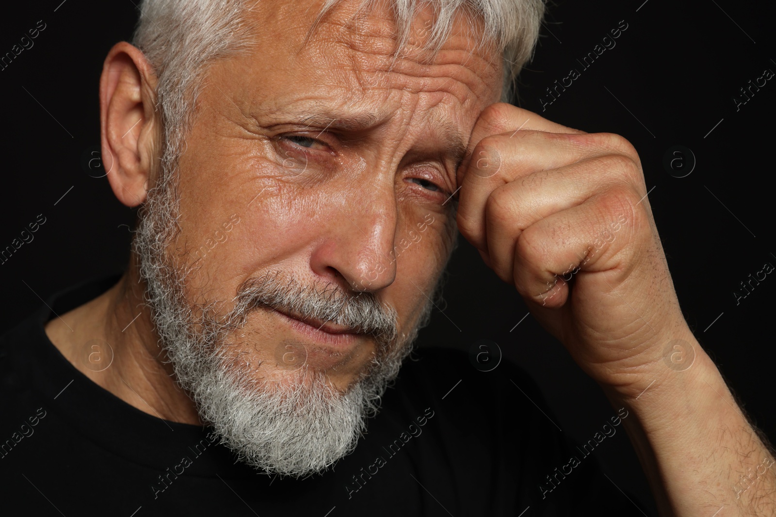 Photo of Sad senior man crying on black background, closeup