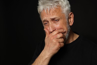 Photo of Sad senior man crying on black background. Space for text