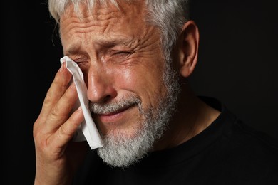 Photo of Sad senior man crying on black background, closeup