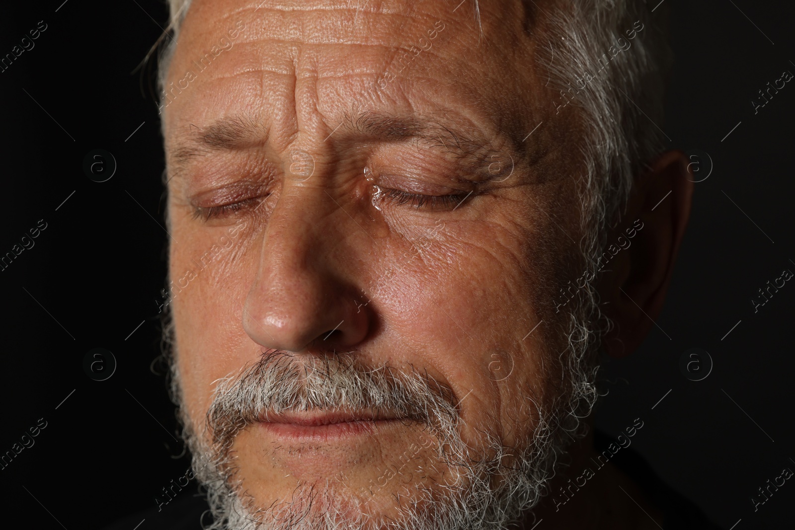 Photo of Sad senior man crying on black background, closeup