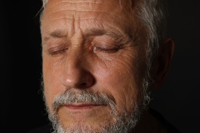 Photo of Sad senior man crying on black background, closeup