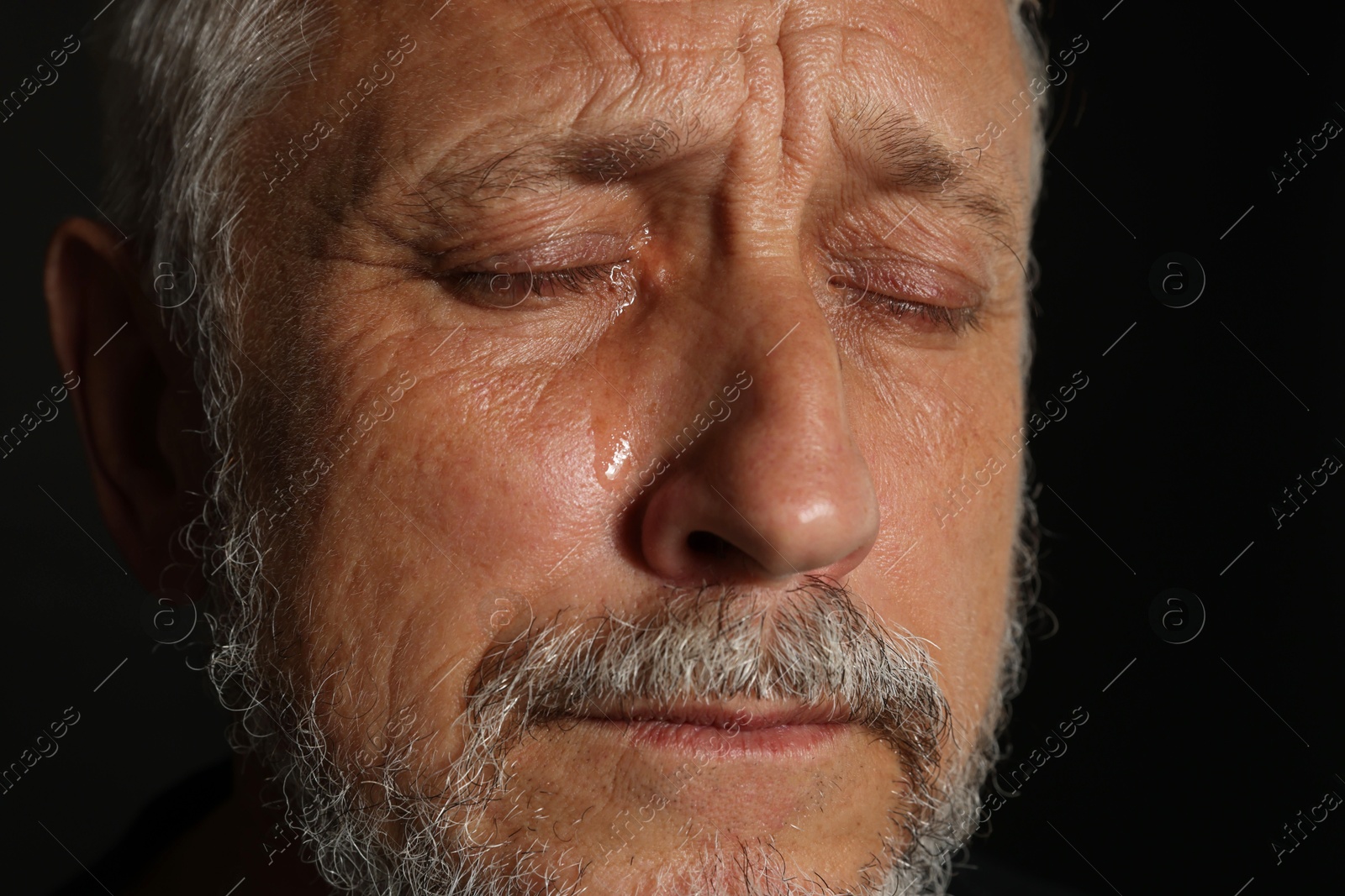 Photo of Sad senior man crying on black background, closeup