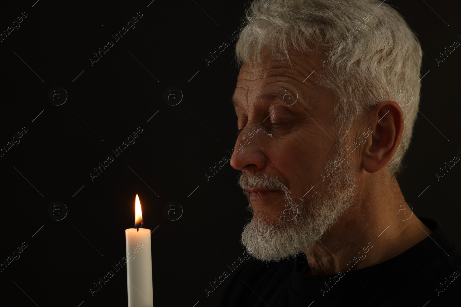 Photo of Sad senior man with burning candle crying on black background, space for text. Grieving loss