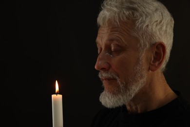 Photo of Sad senior man with burning candle crying on black background, space for text. Grieving loss