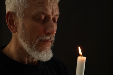 Photo of Sad senior man with burning candle crying on black background. Grieving loss