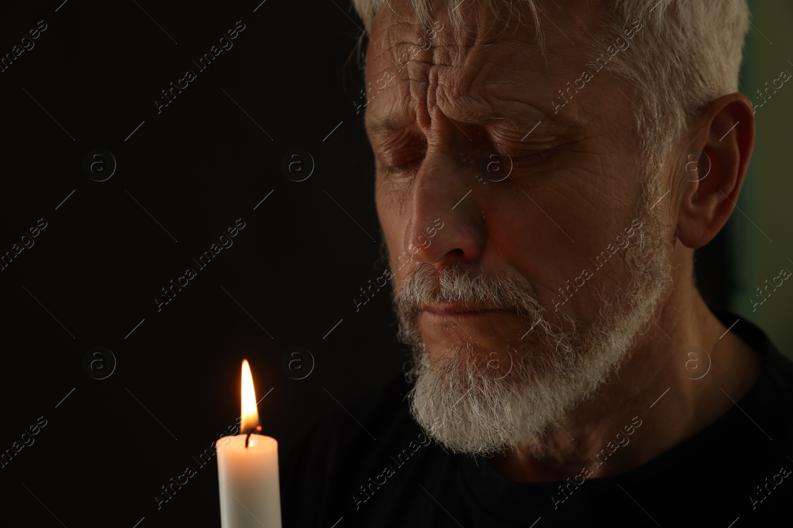 Photo of Sad senior man with burning candle crying on black background. Grieving loss