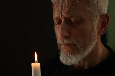 Photo of Sad senior man with burning candle crying on black background. Grieving loss