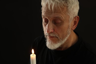 Photo of Sad senior man with burning candle crying on black background, space for text. Grieving loss