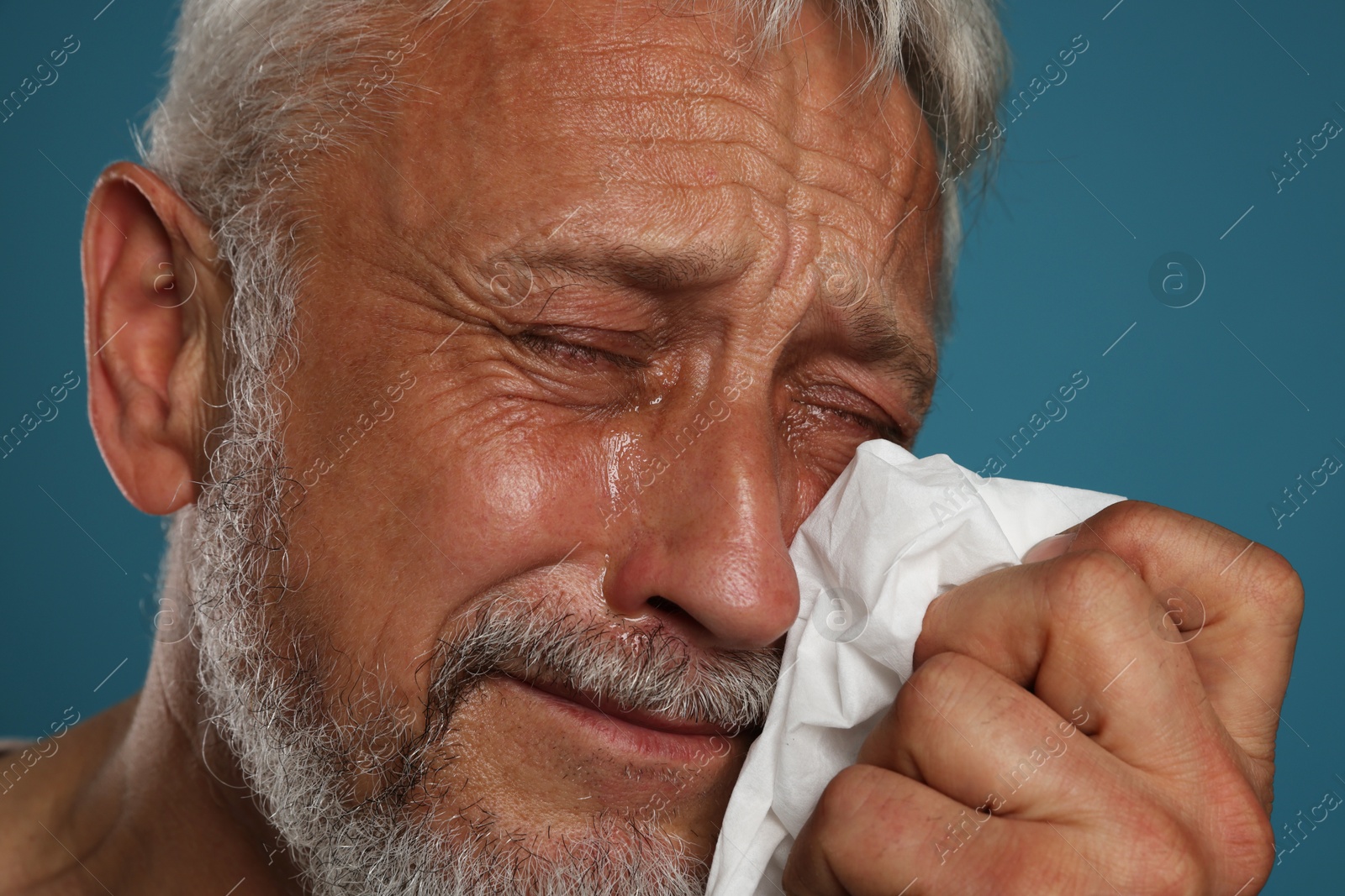 Photo of Sad senior man crying on blue background, closeup