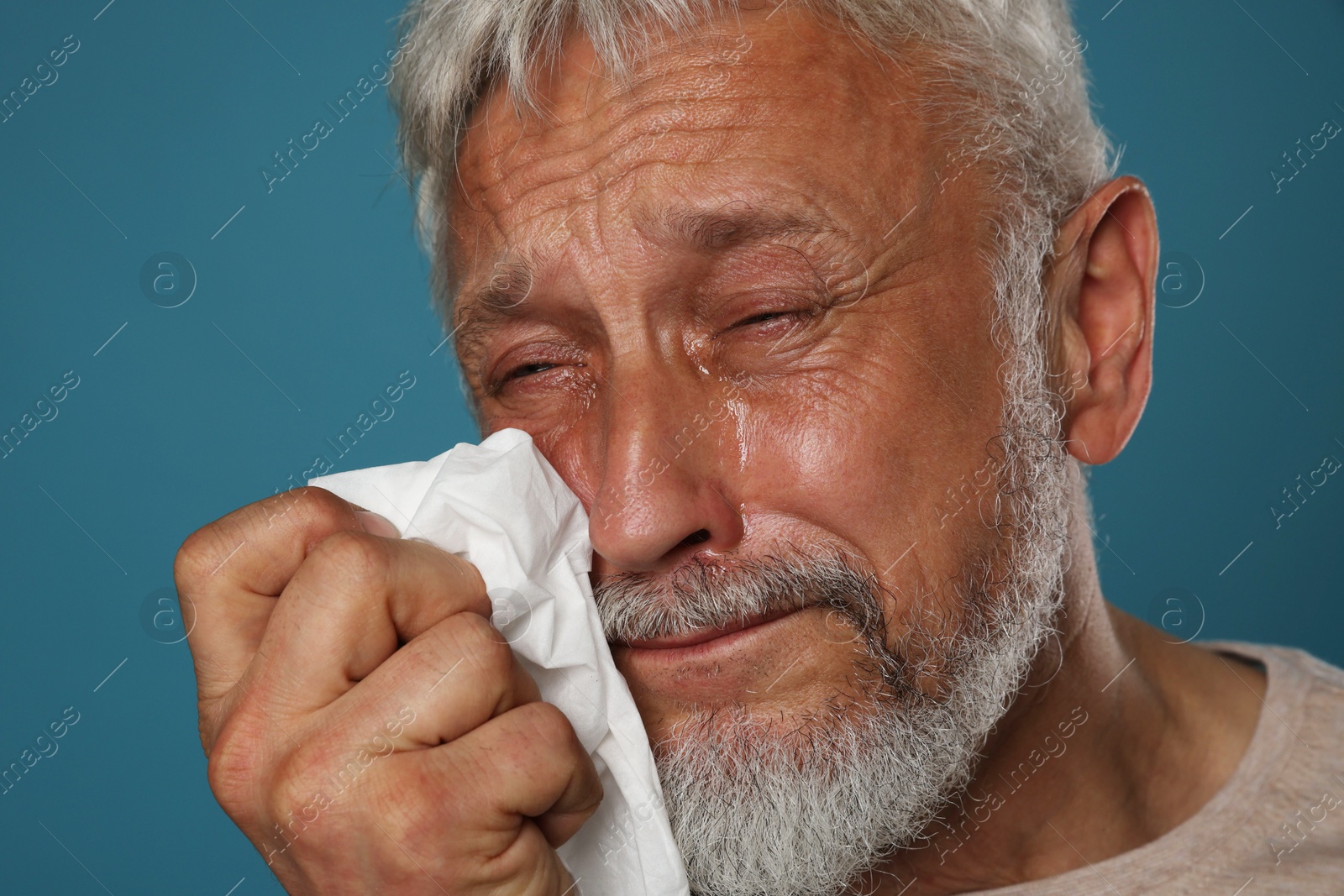 Photo of Sad senior man crying on blue background, closeup