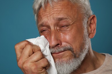 Photo of Sad senior man crying on blue background, closeup