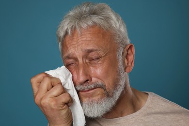 Photo of Sad senior man crying on blue background, closeup