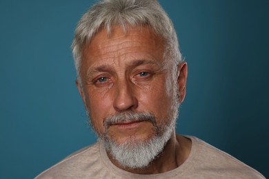 Photo of Sad senior man crying on blue background, closeup