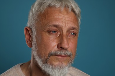 Photo of Sad senior man crying on blue background, closeup